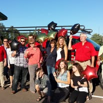 Group of people celebrating with balloons in front of a vehicle on a sunny day.