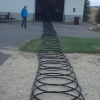 Man walks toward a building with a large coiled black hose on the ground.