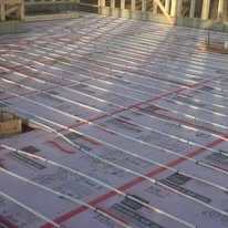 Radiant floor heating system with white tubing laid across insulation panels in a building under construction.