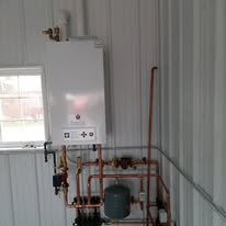 Wall-mounted water heater with copper pipes in a white-walled room.