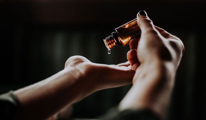 Handen gieten olie uit een bruine fles in de handpalm. Donkere omgeving.