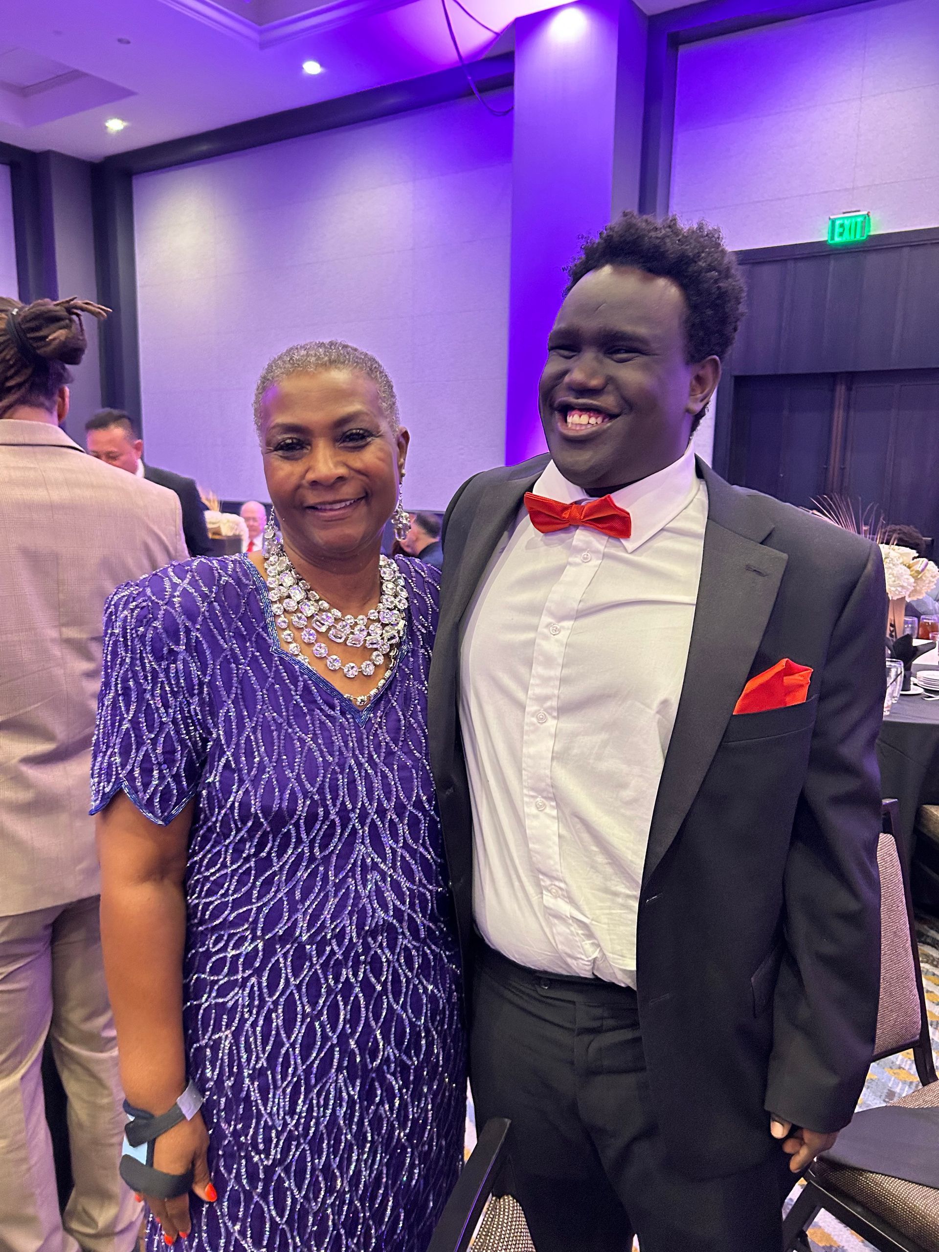 Woman in purple dress and man in tuxedo smiling together at an event.