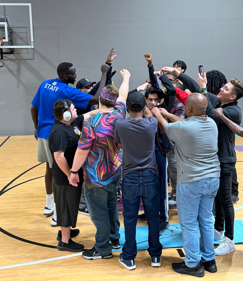 People in a gym practicing basketball drills, holding basketballs, some are doing lunges.