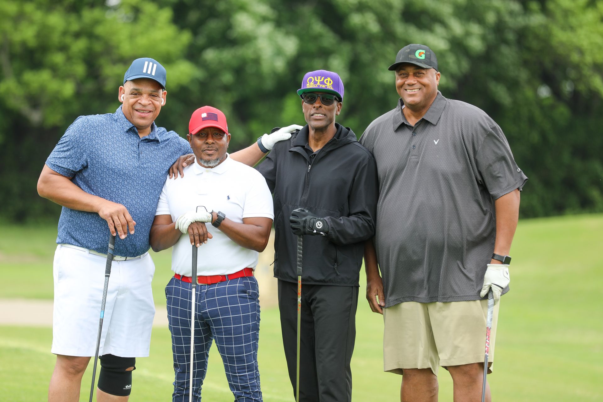 Four men on a golf course smiling, posing with golf clubs.