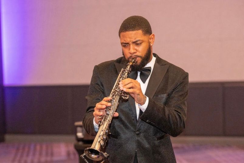 Man in tuxedo playing a saxophone, performing at an event.