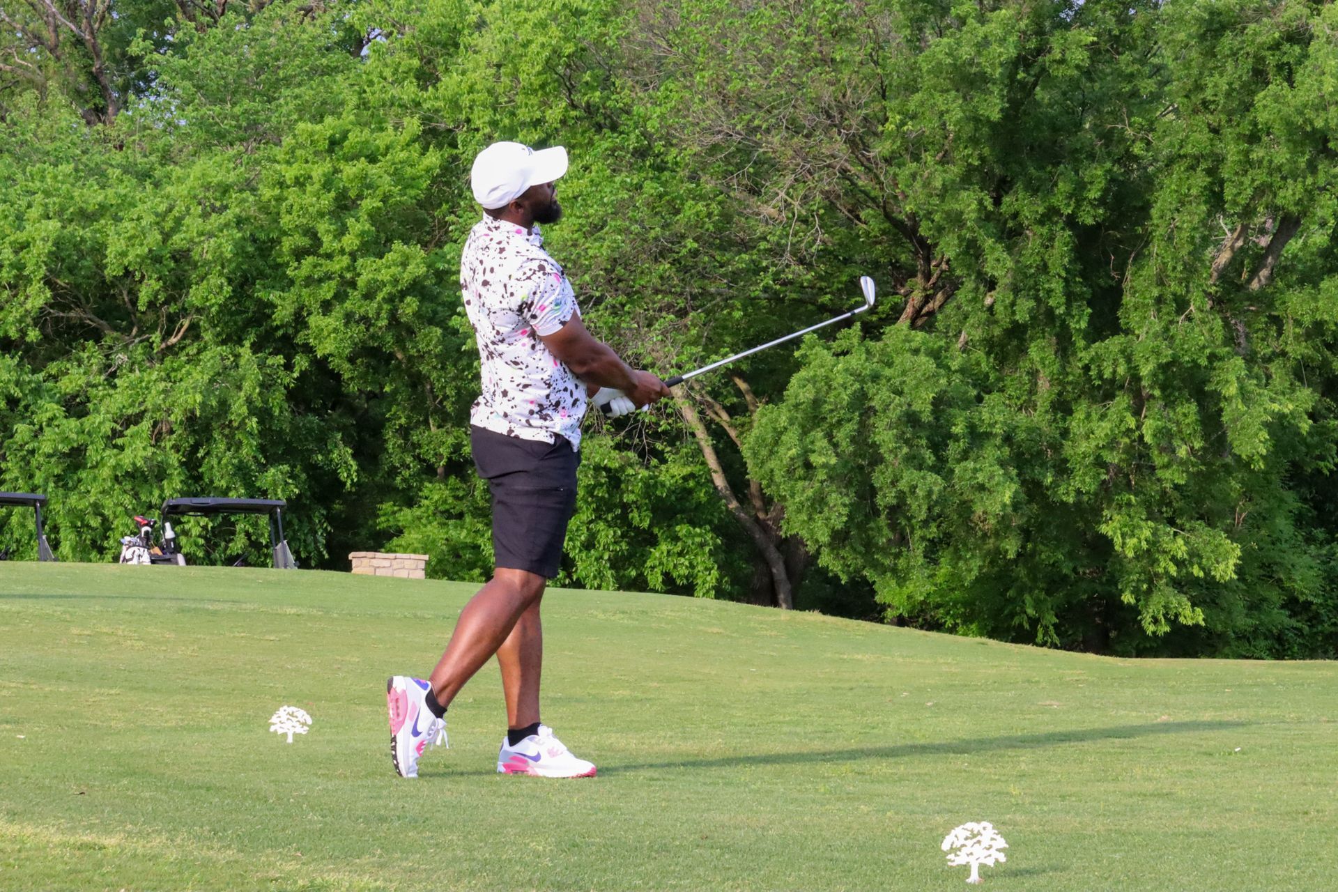 Man in white hat and floral shirt playing golf on green.