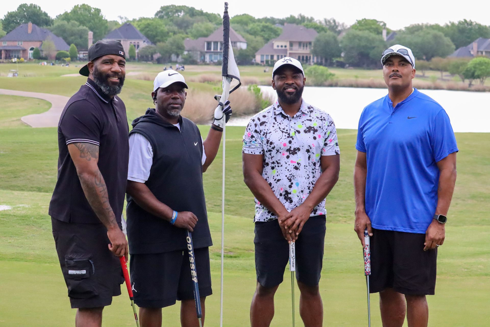 Four Black men on a golf course, smiling. They are standing on the green near a flag.