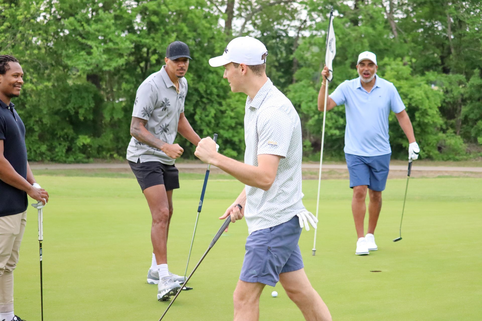 Four men on a golf course celebrate near the green. One man raises his fist.
