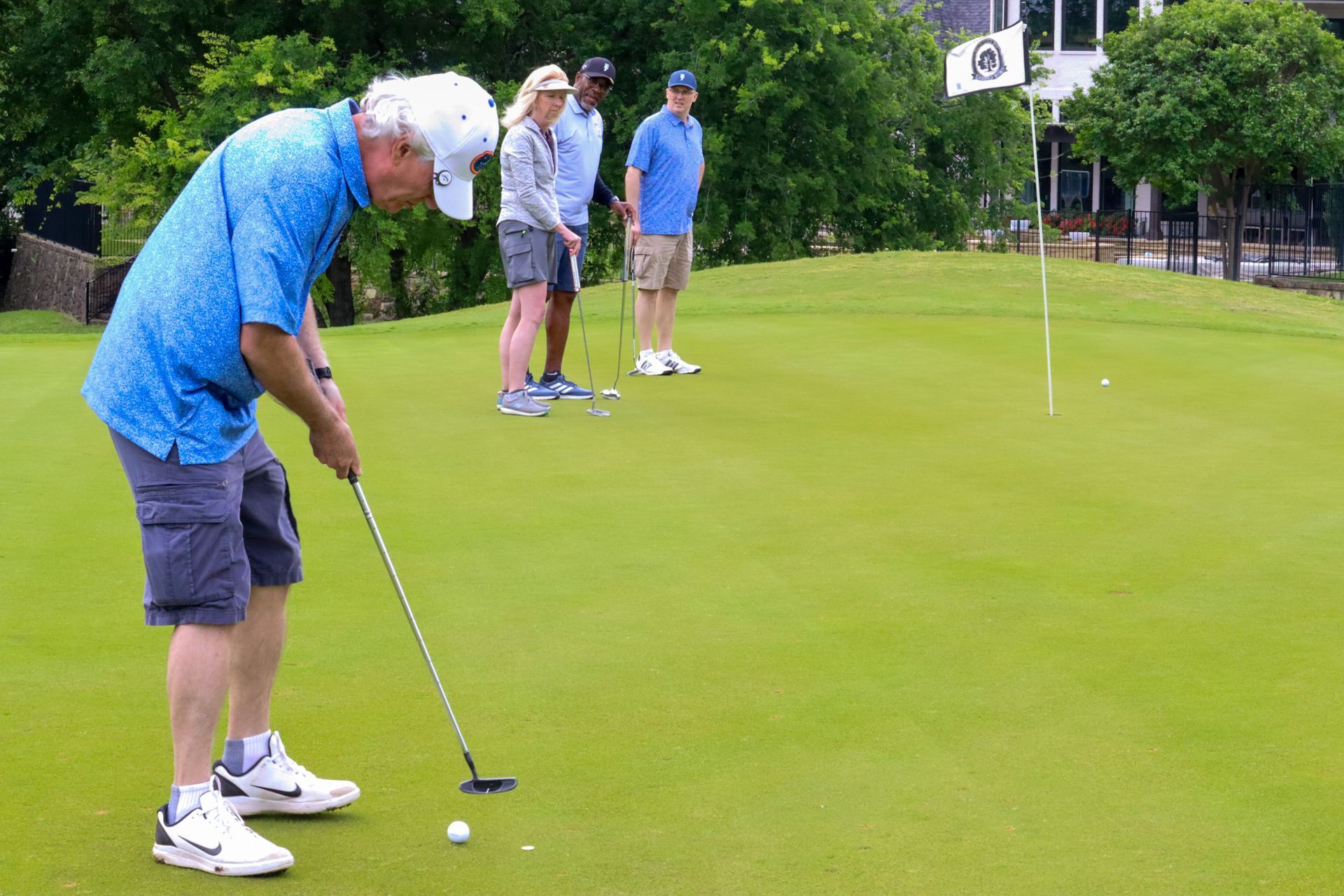 Man putting golf ball on green, other players watch in background.