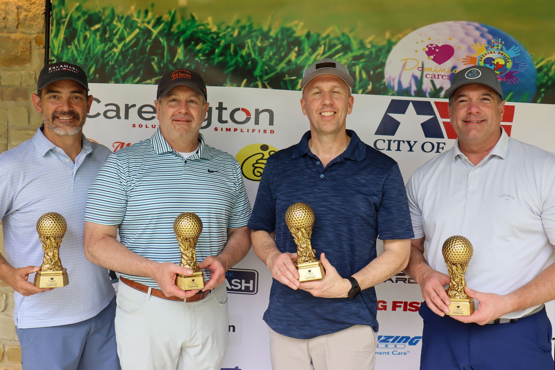 Four men in golf attire holding trophies after an event; a banner in the background.