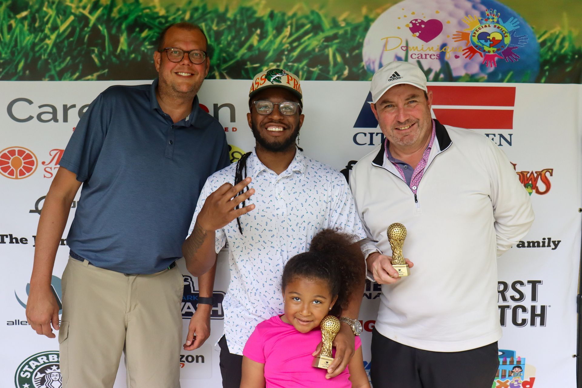 Four people, including a young girl, pose with trophies after a golf event.