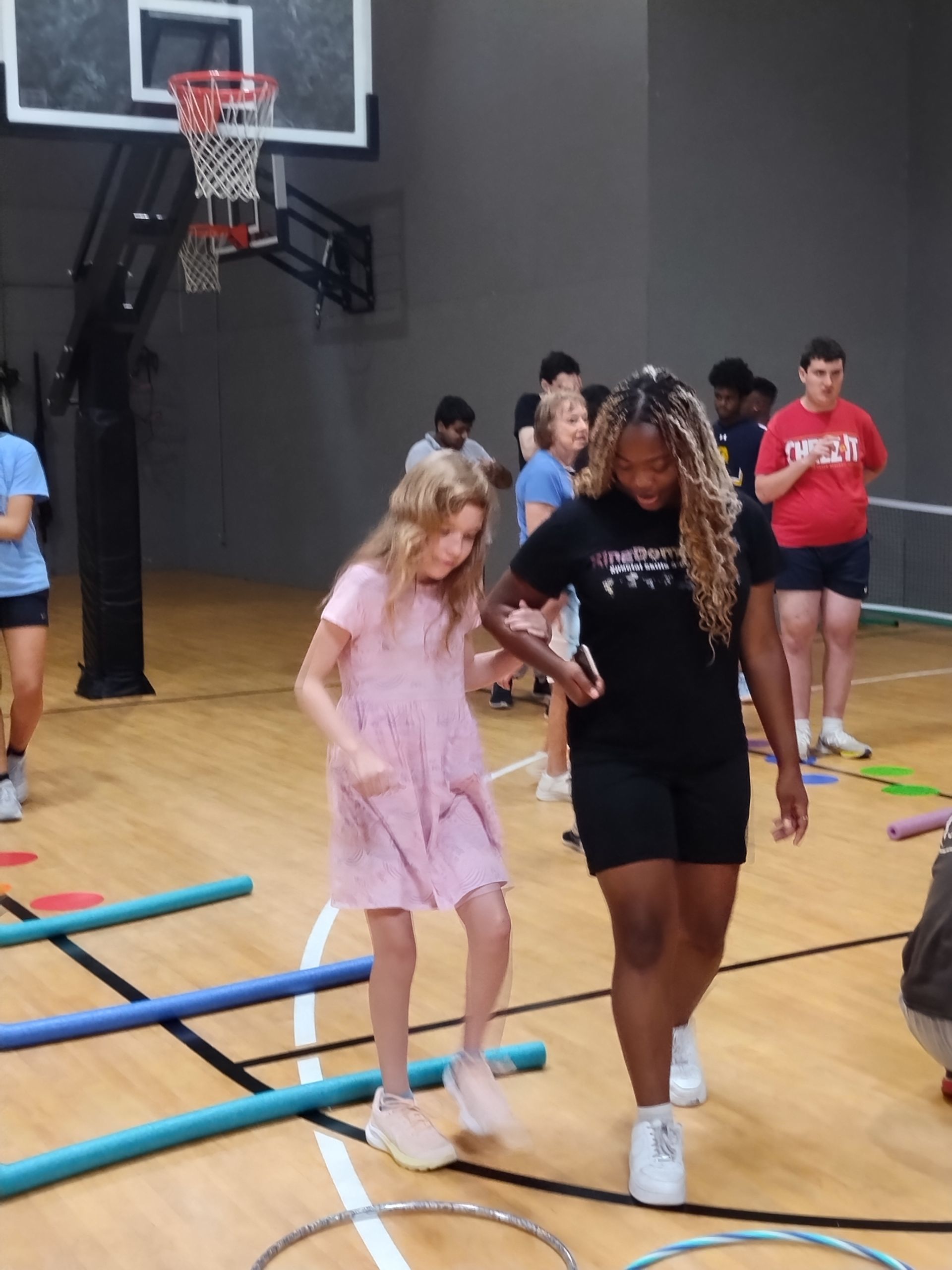 A young girl and woman navigate a floor obstacle course in a gym.