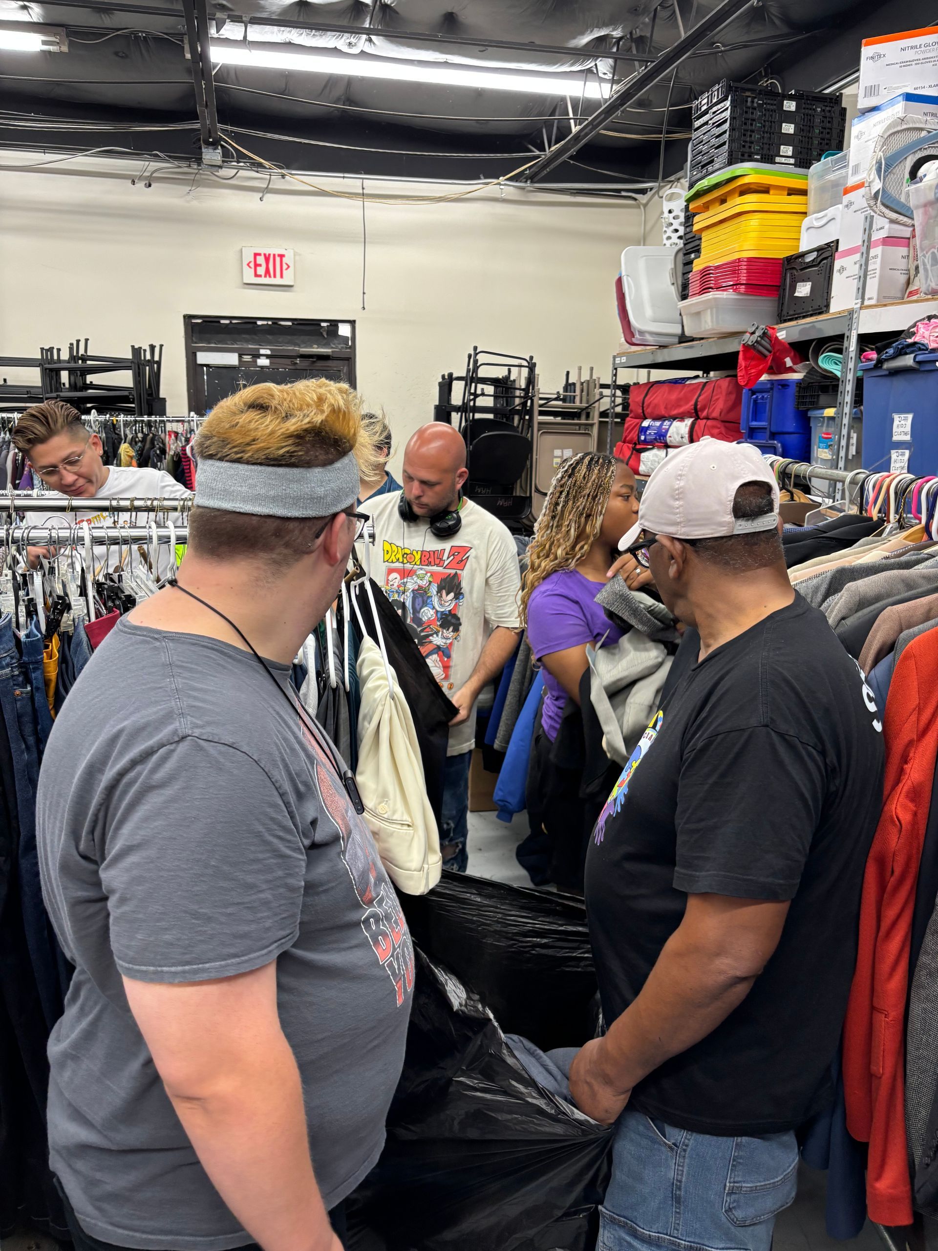People browsing clothes racks in a brightly lit thrift store.