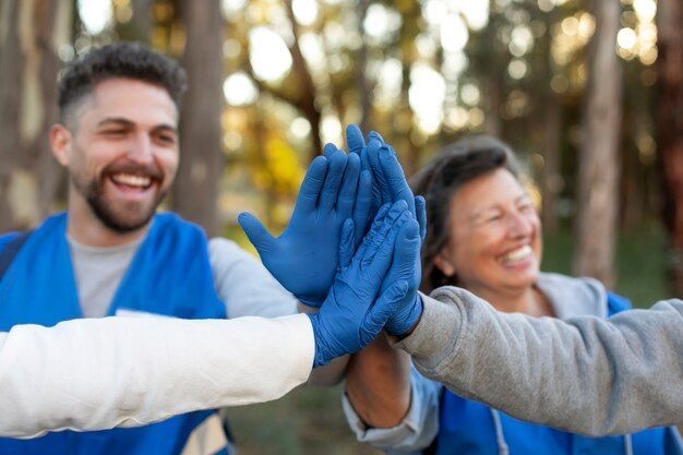Group of volunteers wearing blue vests, smiling, high-fiving each other outdoors.
