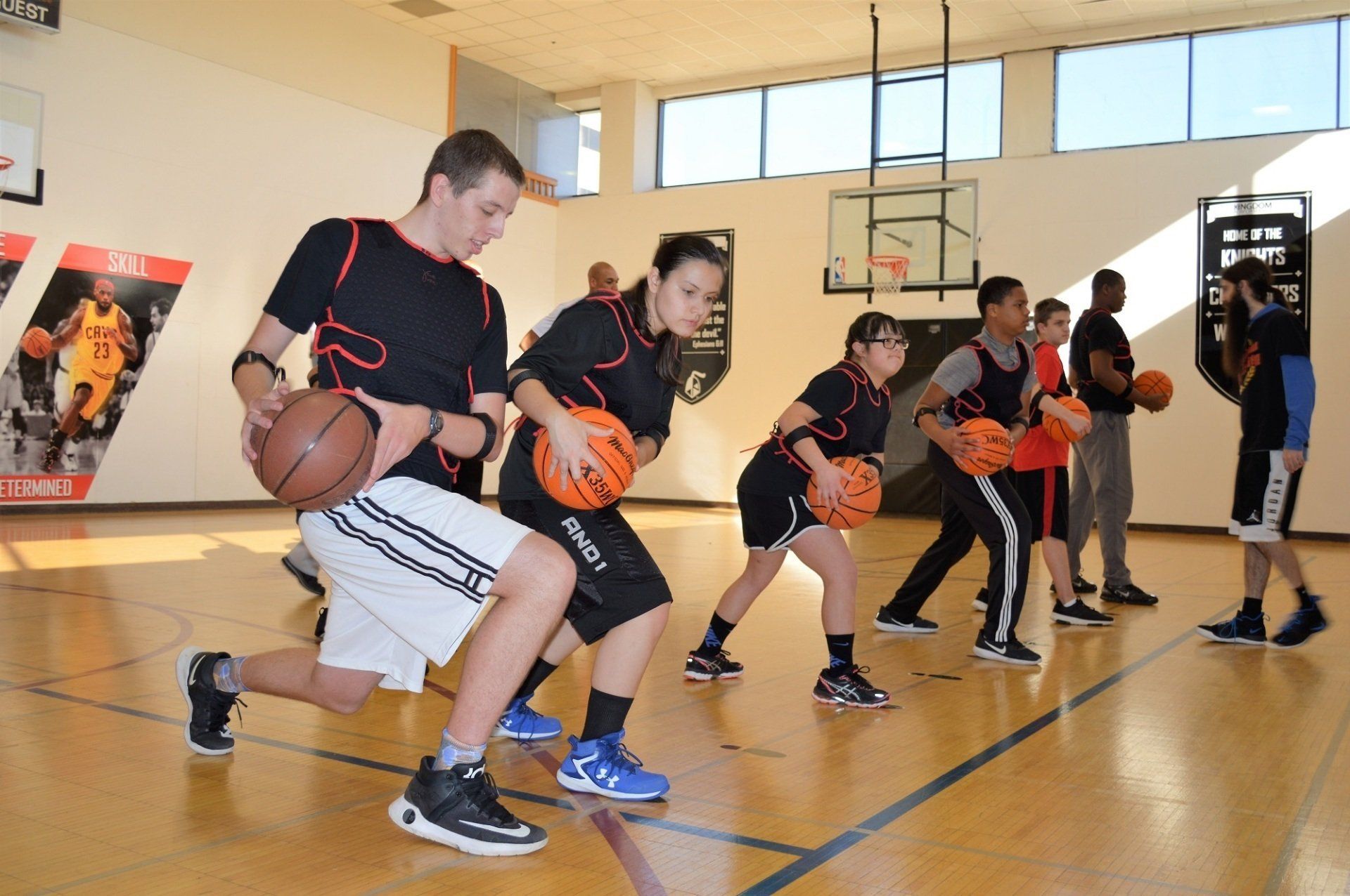 People in a gym practice basketball drills, dribbling while lunging.