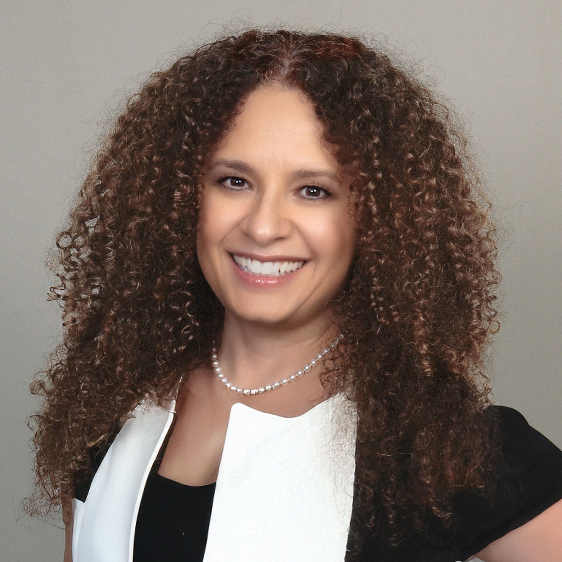 A woman with curly hair is smiling and wearing a white shirt.