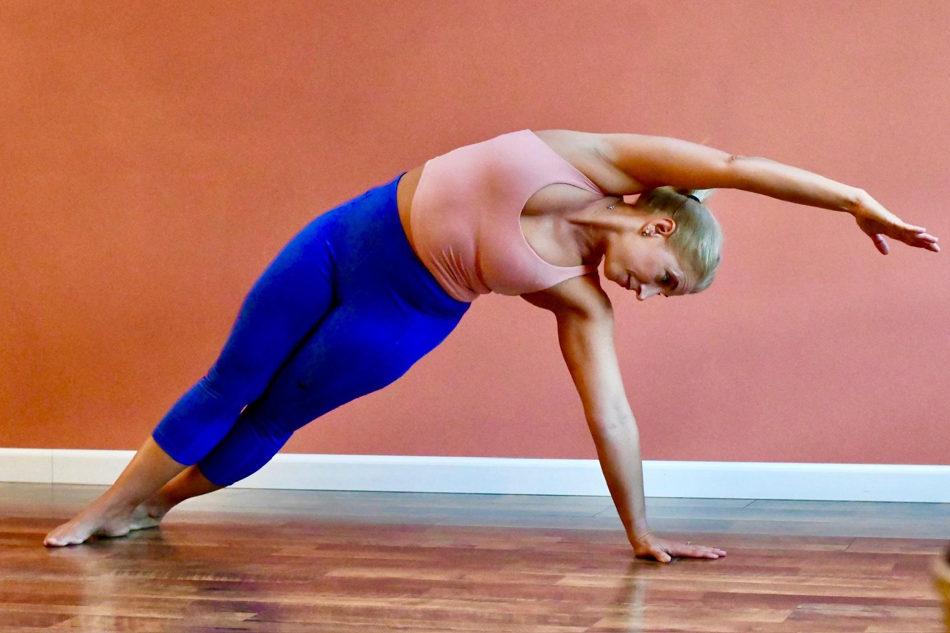 Heidi in a standing side bend, one hand reaching to the floor and the other arm extended overhead