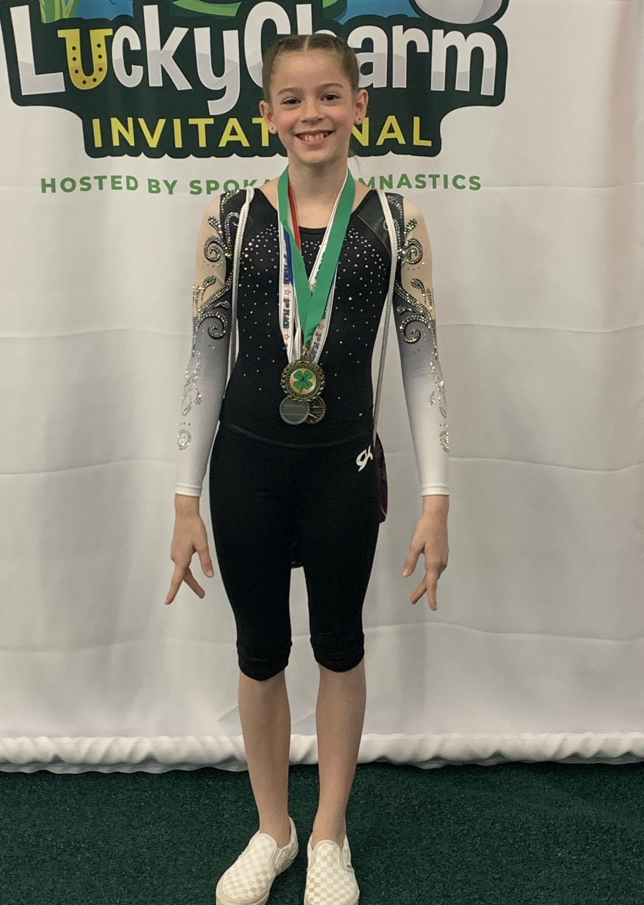 a young girl wearing a medal is standing in front of a lucky charm invitational banner .