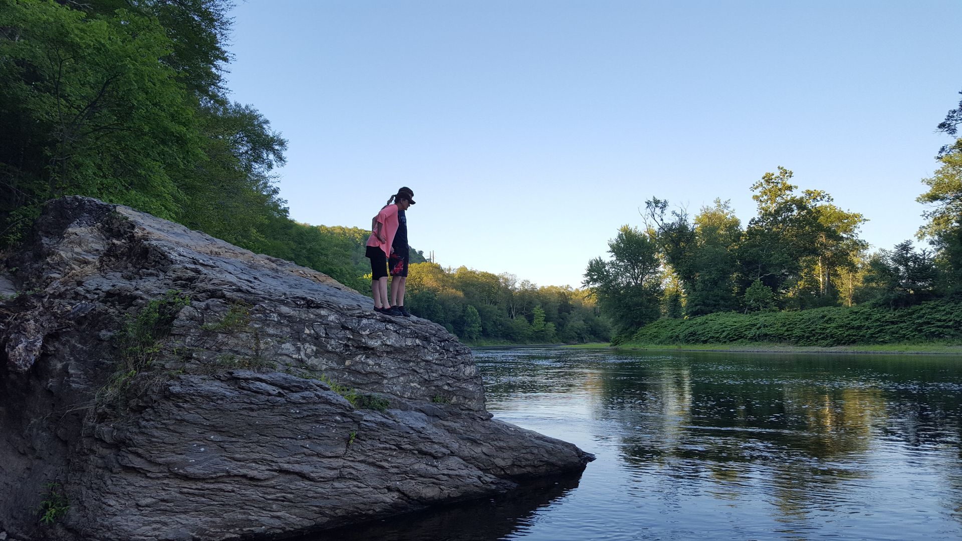 A woman is standing on a rock overlooking a river.