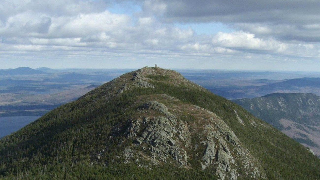 A mountain with trees on it and a cloudy sky in the background. A mountain with trees on it and a cloudy sky in the background.