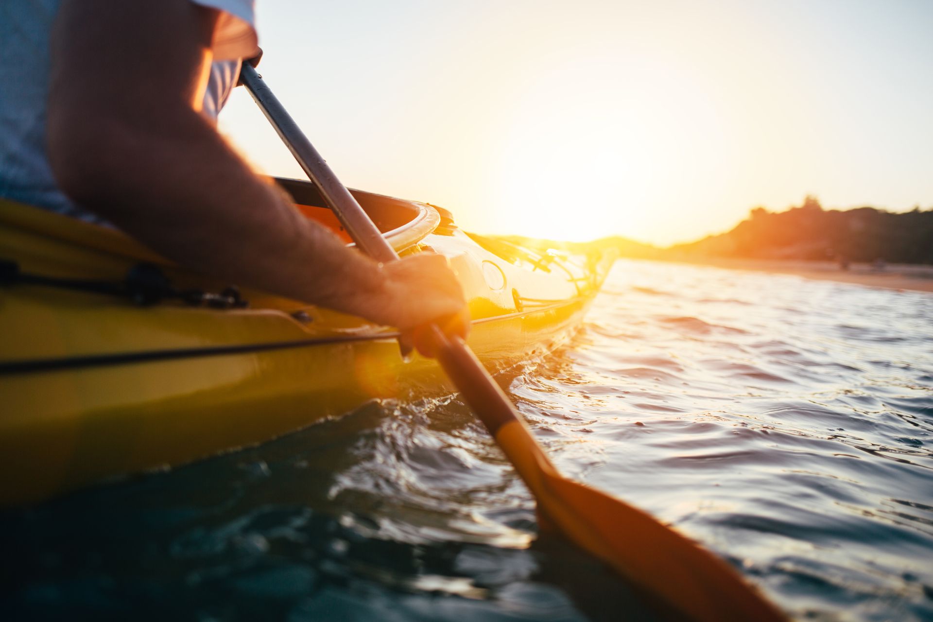 Kayaker paddling a yellow kayak on calm water at sunset