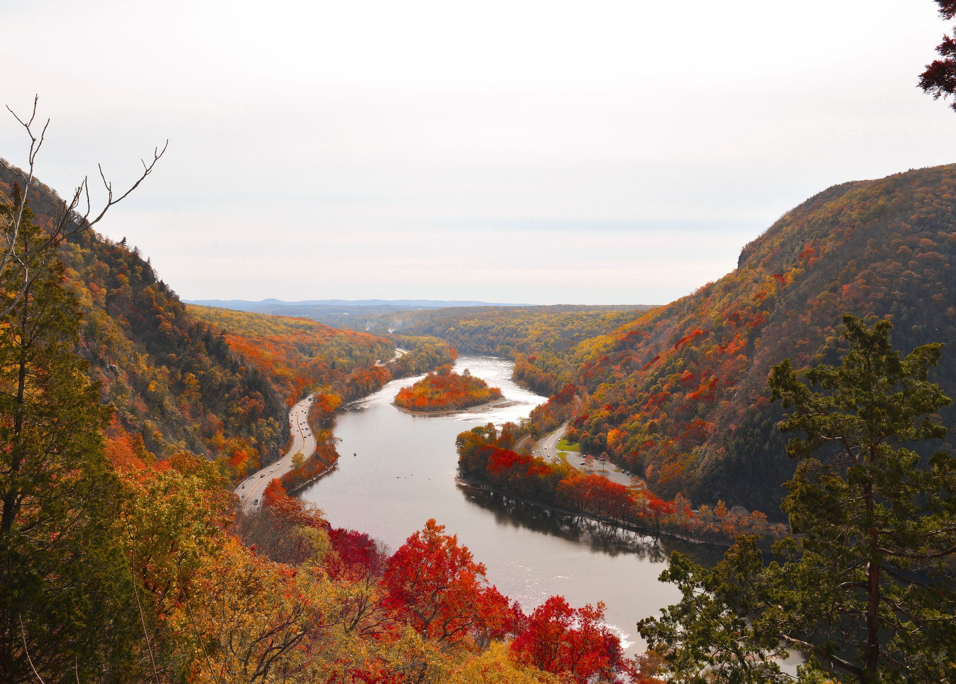 Winding river through a colorful autumn valley between rocky hills under a pale sky