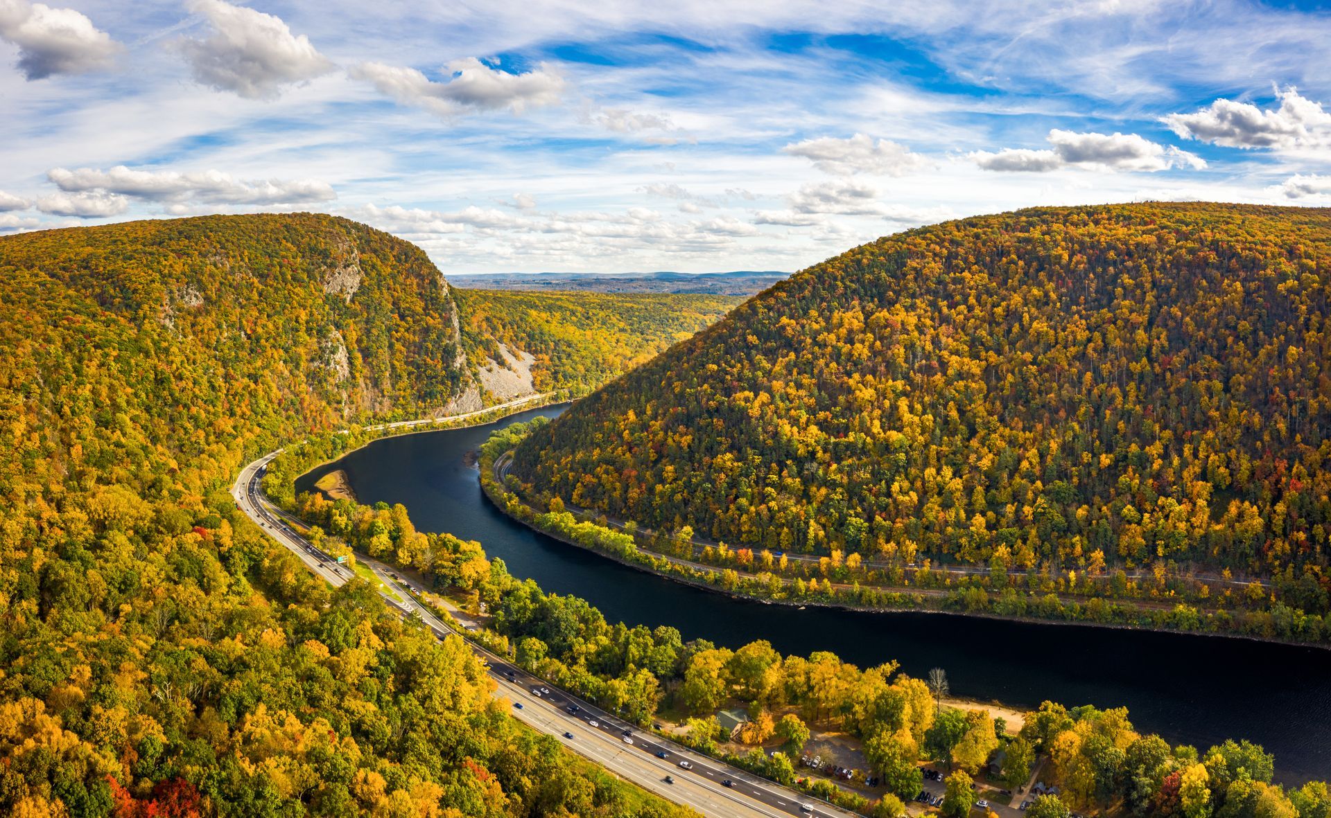 Winding river through forested hills in autumn with a road along the water