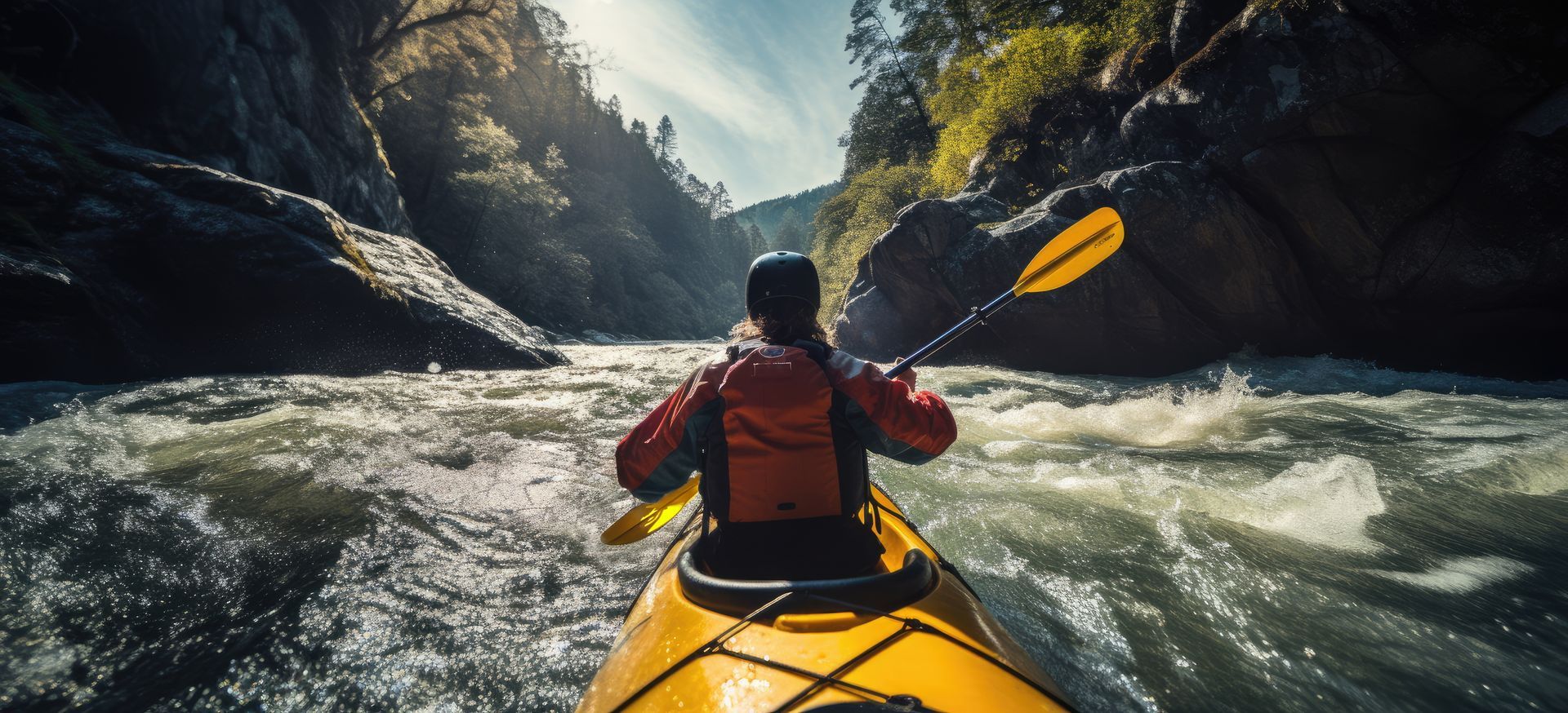 Kayaker paddles a yellow kayak through a rocky river gorge under bright sunlight