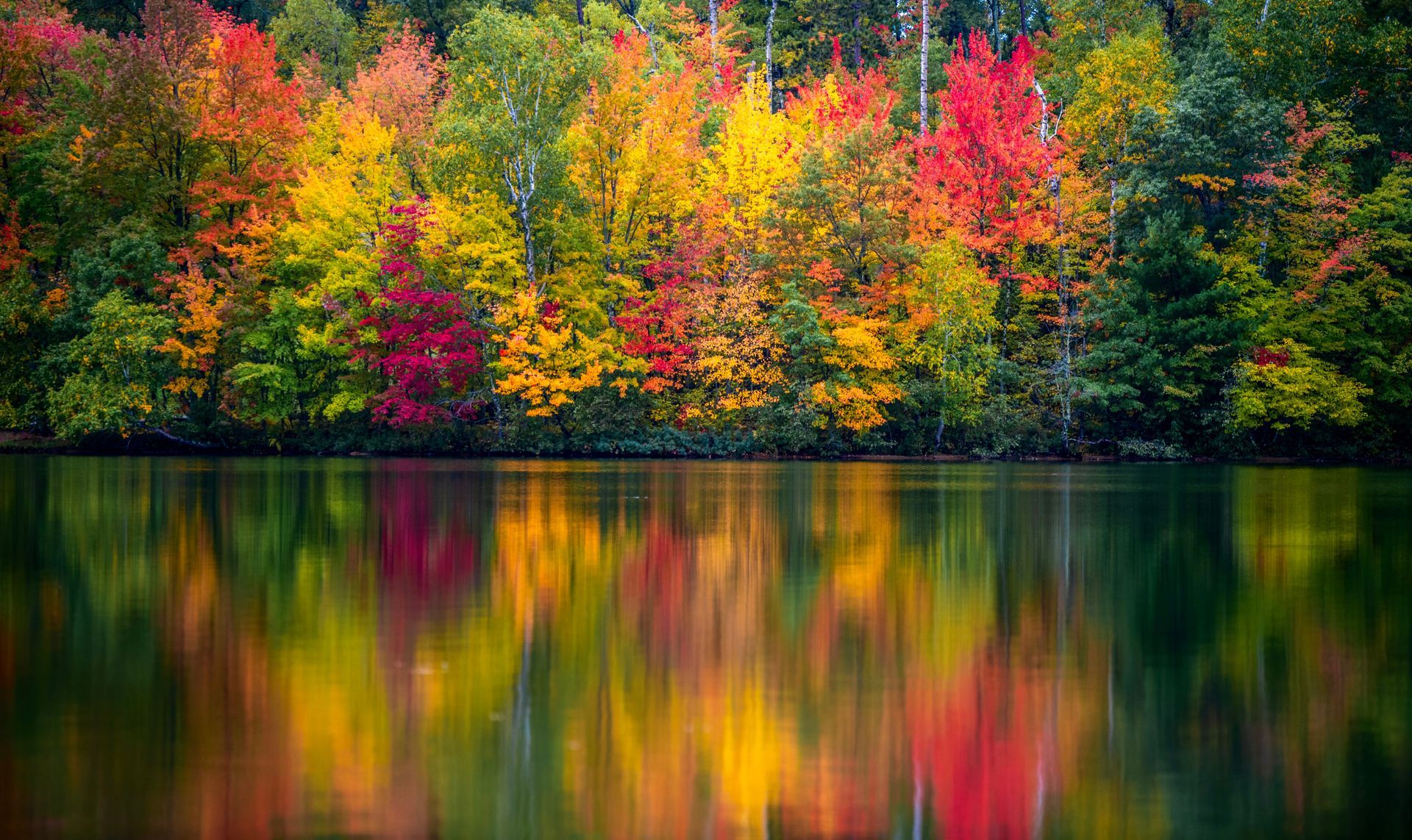 Autumn trees in vivid red, yellow, and green reflected in a calm lake