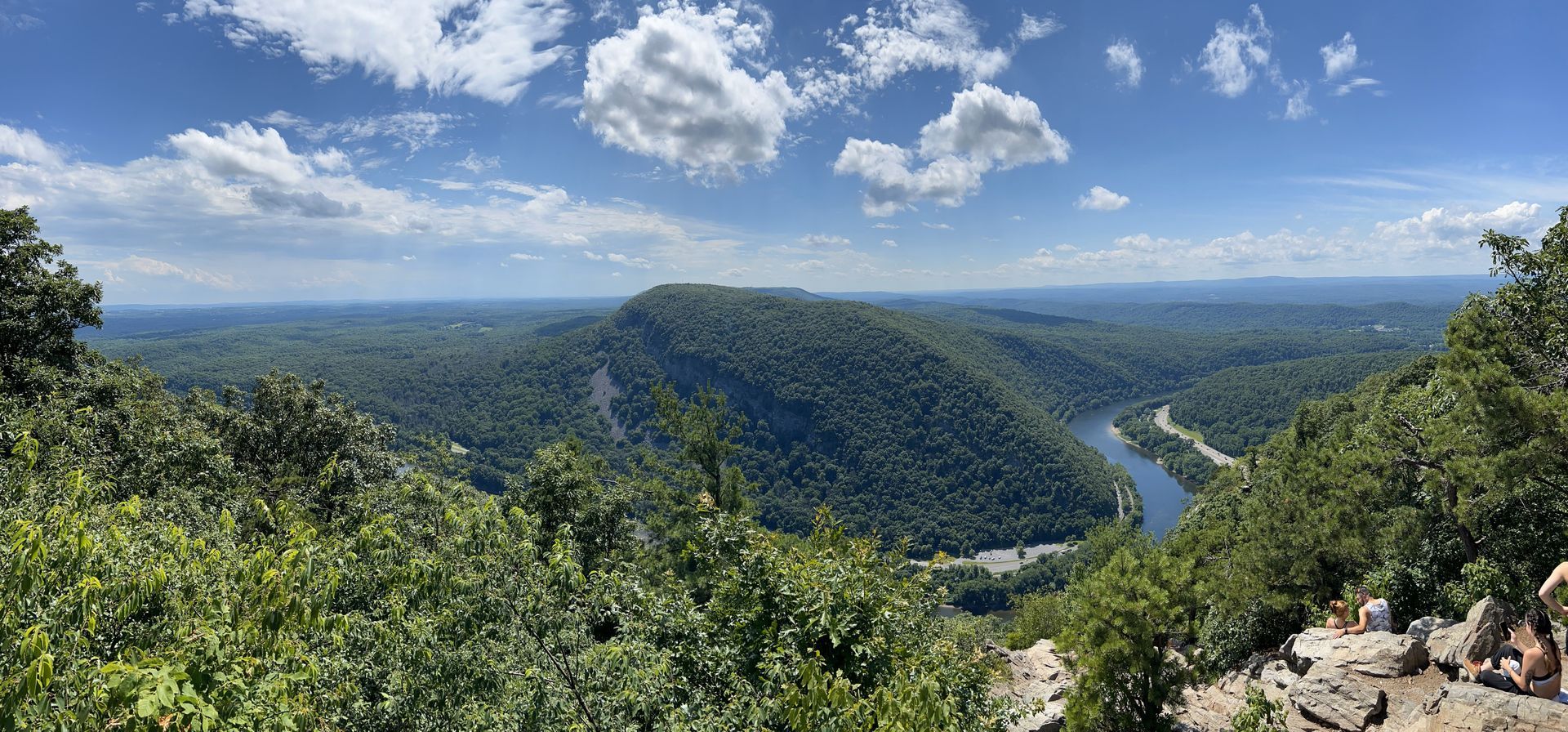 Panoramic view of a lush green river valley under a blue sky with scattered clouds