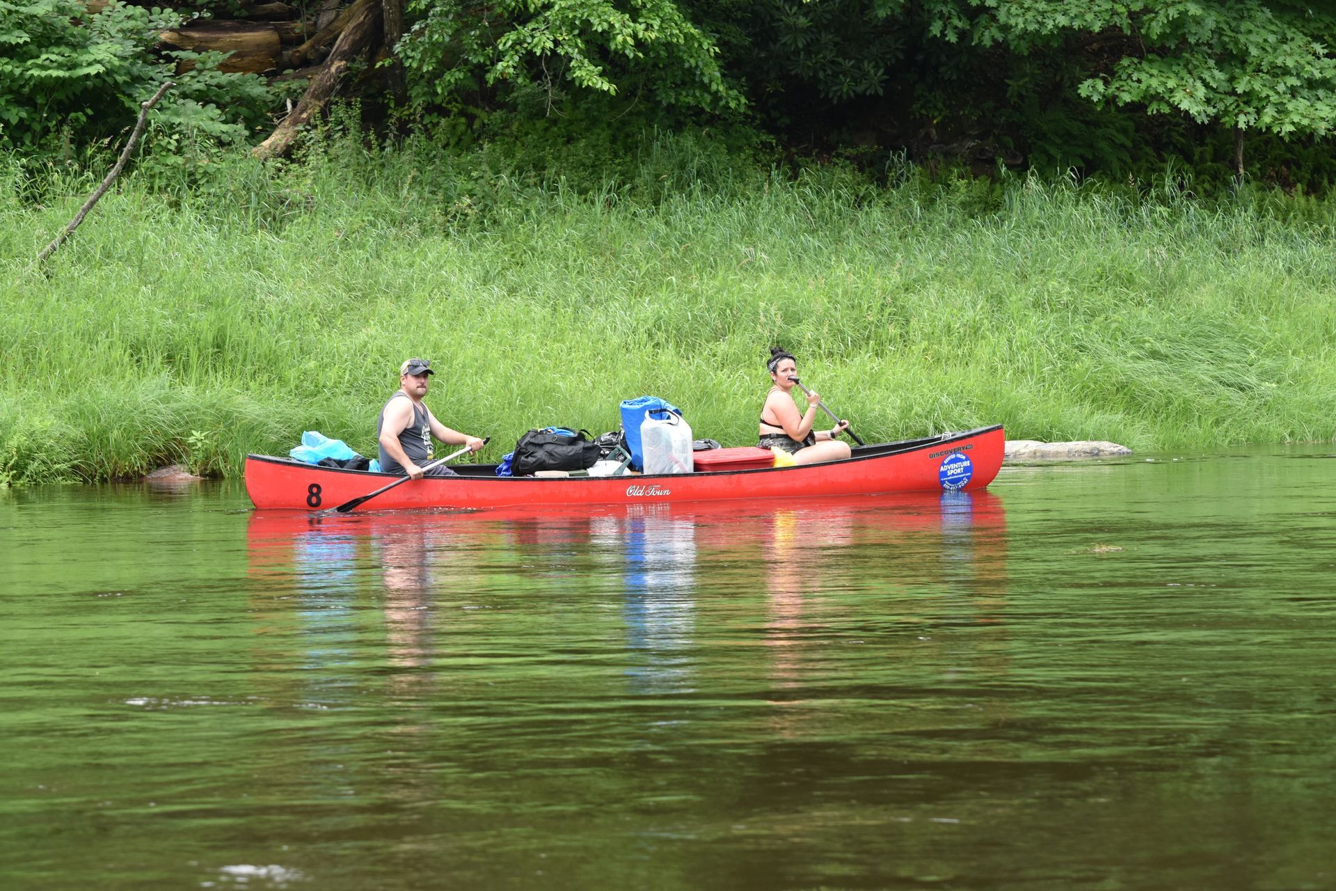 Two people are in a red adventure sports canoe on a river.