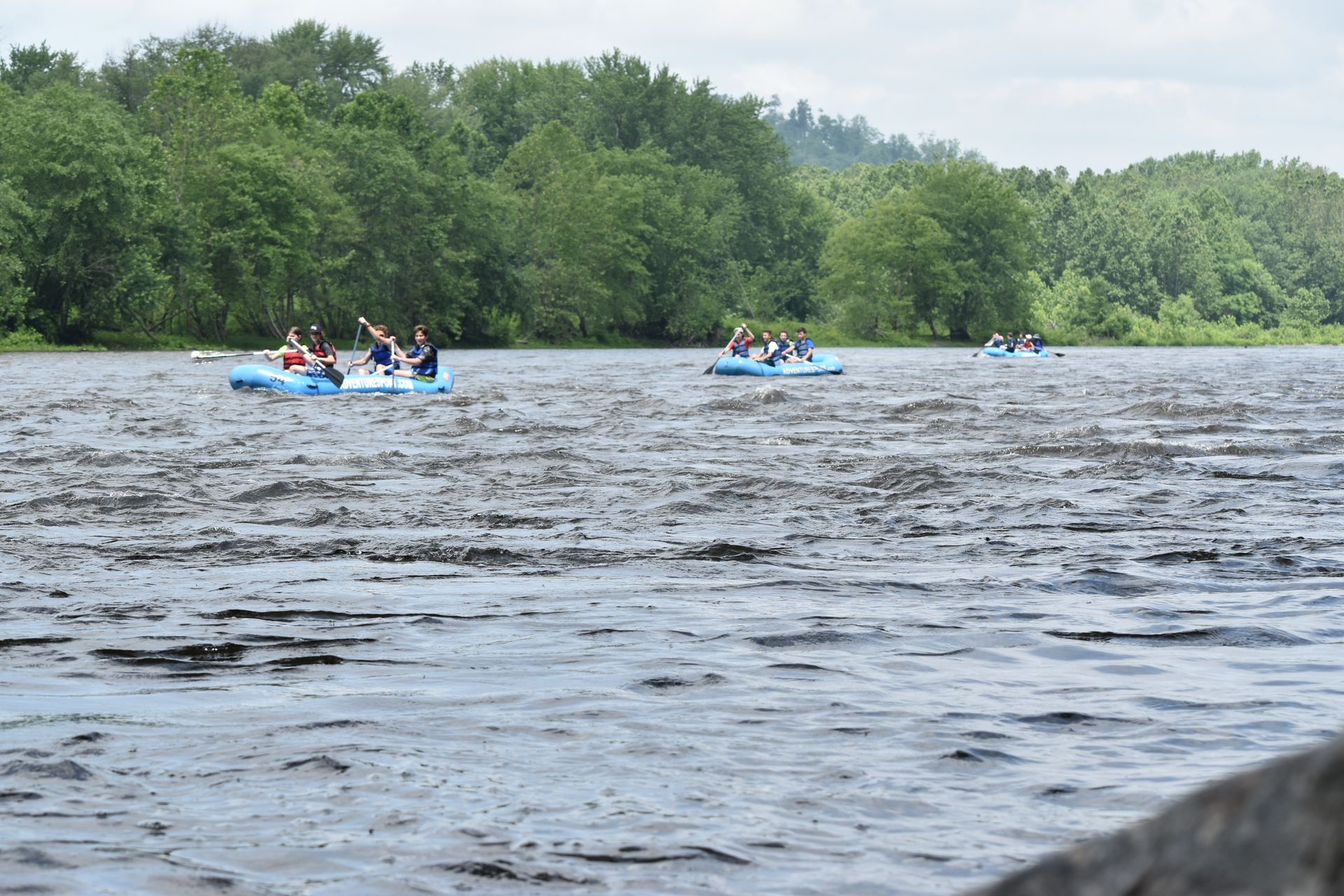 A group of people are rowing adventure sports rafts down a river.