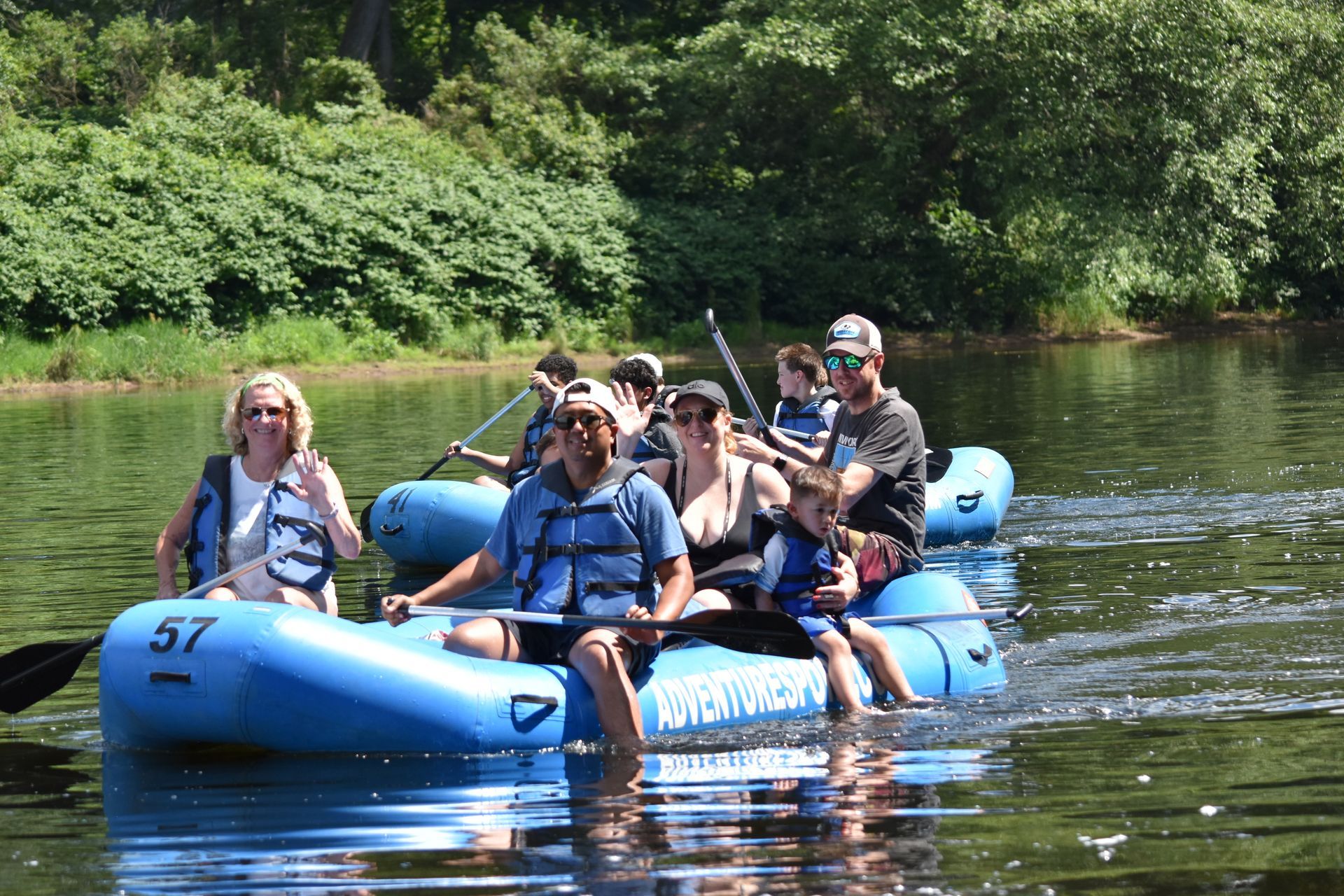 People rafting on a blue inflatable raft on a calm river, surrounded by green trees