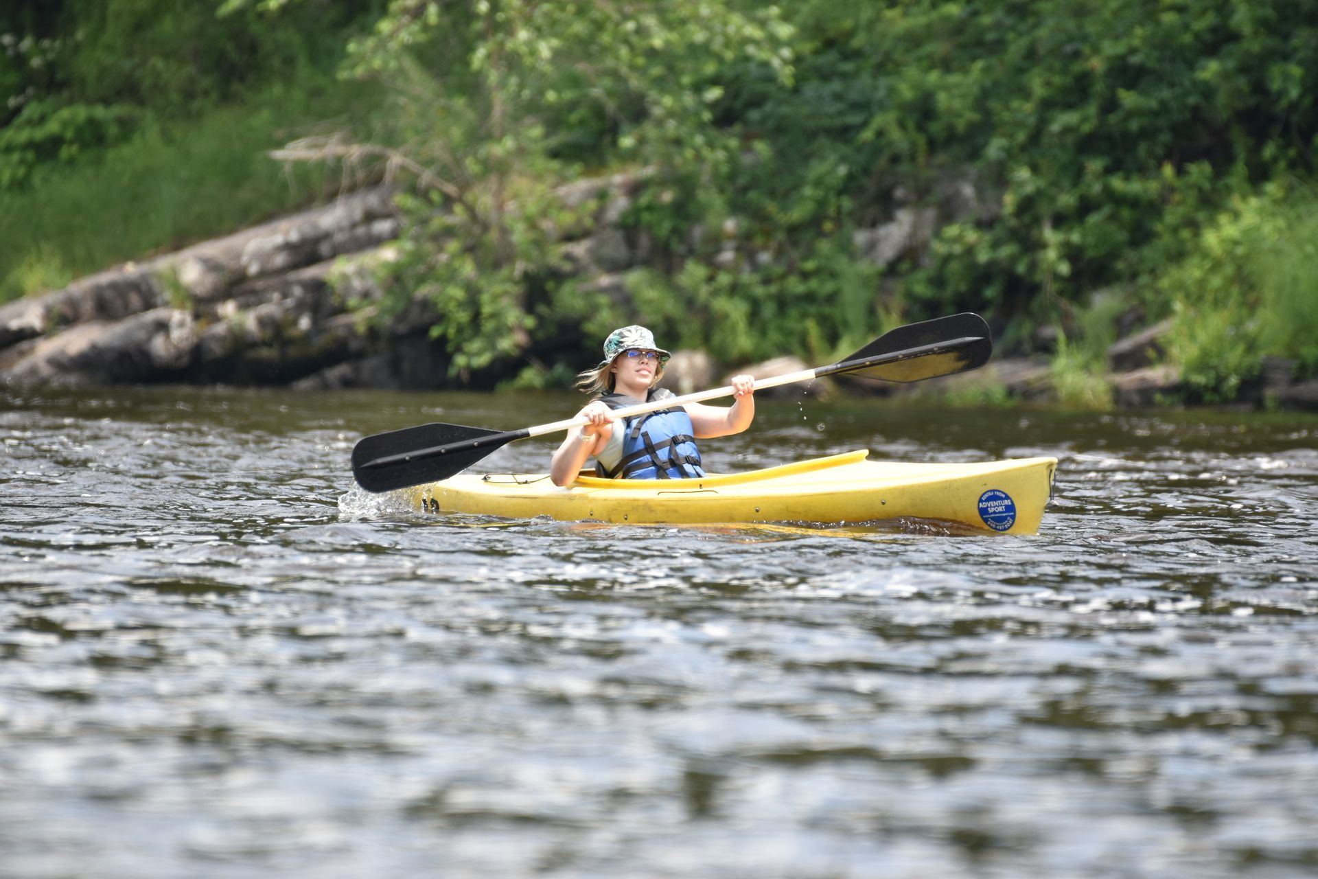 A woman is paddling a yellow adventure sports kayak on a river.