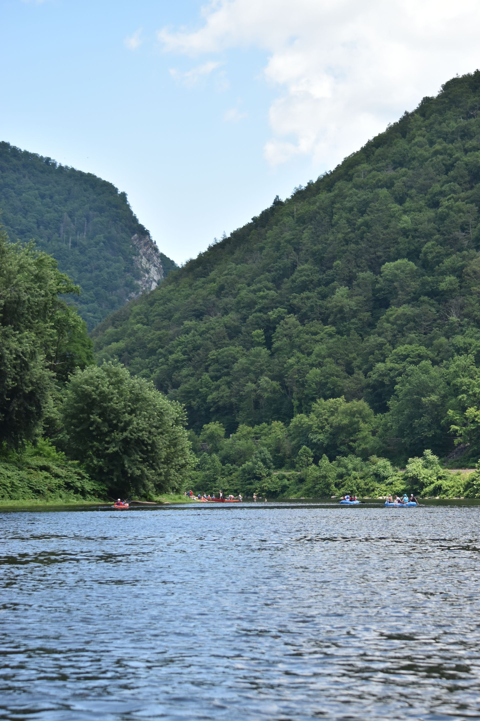 A group of people are rowing adventure sports kayaks down a river surrounded by mountains.
