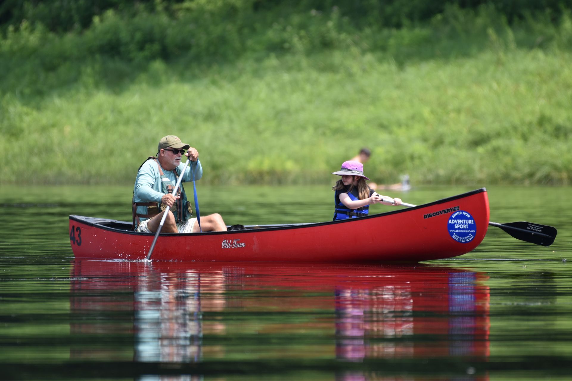A man and a child are paddling a red adventure sports canoe on a lake.