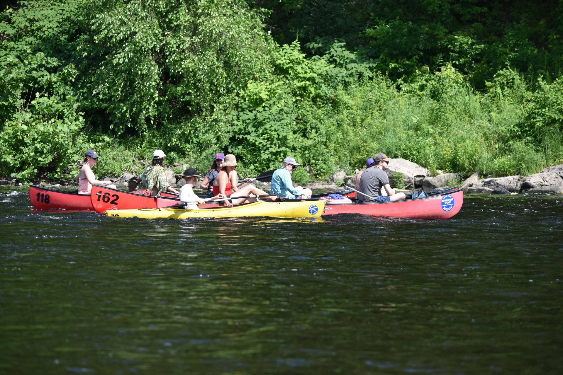A group of people are rowing adventure sports kayaks down a river.