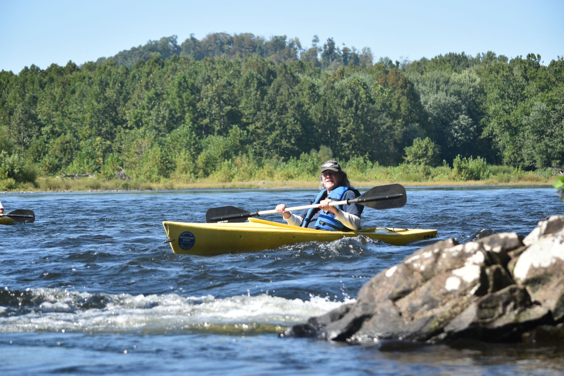 A woman is paddling a yellow adventure sports kayak on a river.