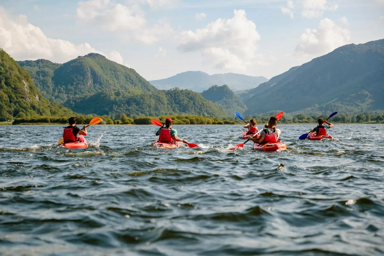 A group of people are kayaking on a lake with mountains in the background. A group of people are kayaking on a lake with mountains in the background.