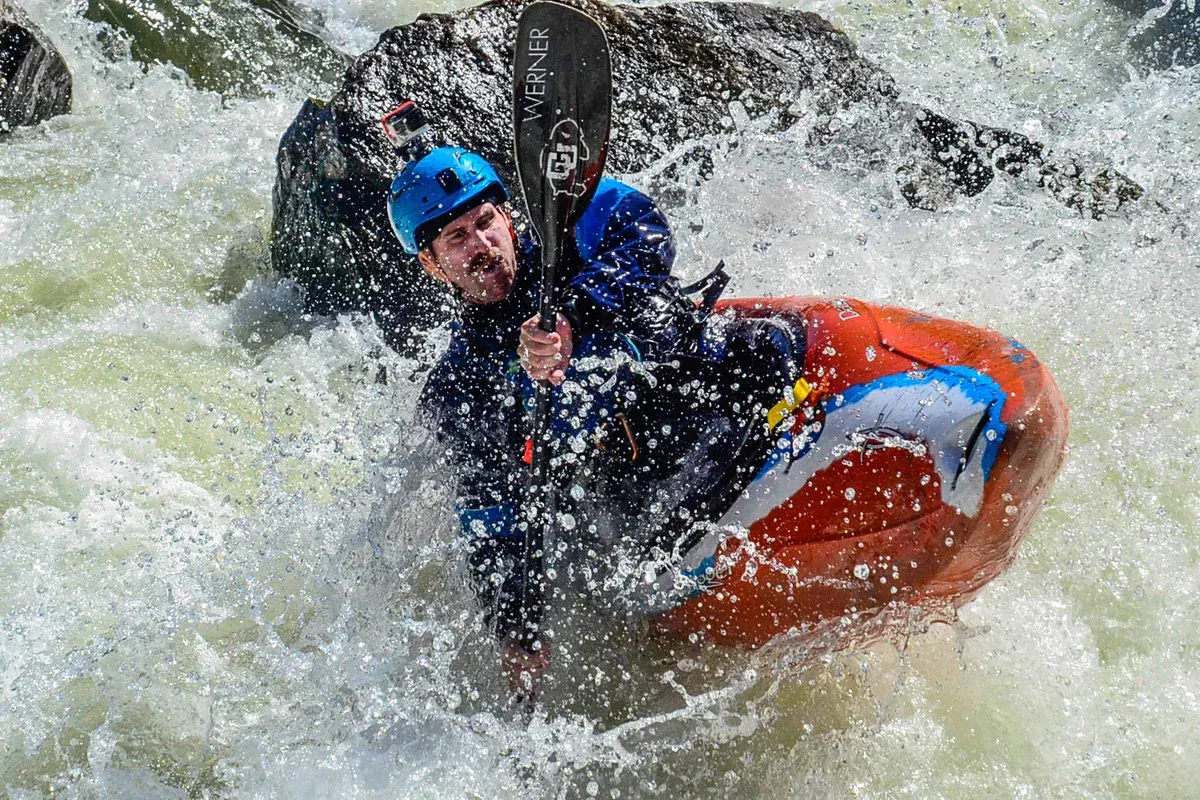 A man is riding a kayak through a river wearing his safety helmet. A man is riding a kayak through a river wearing his safety helmet.