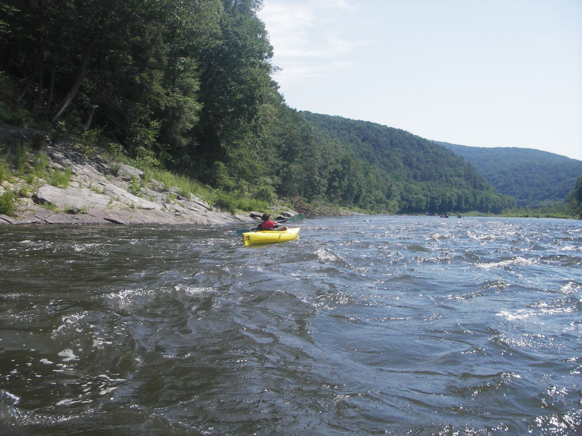 A person with adventure sports in a yellow kayak is paddling down a river