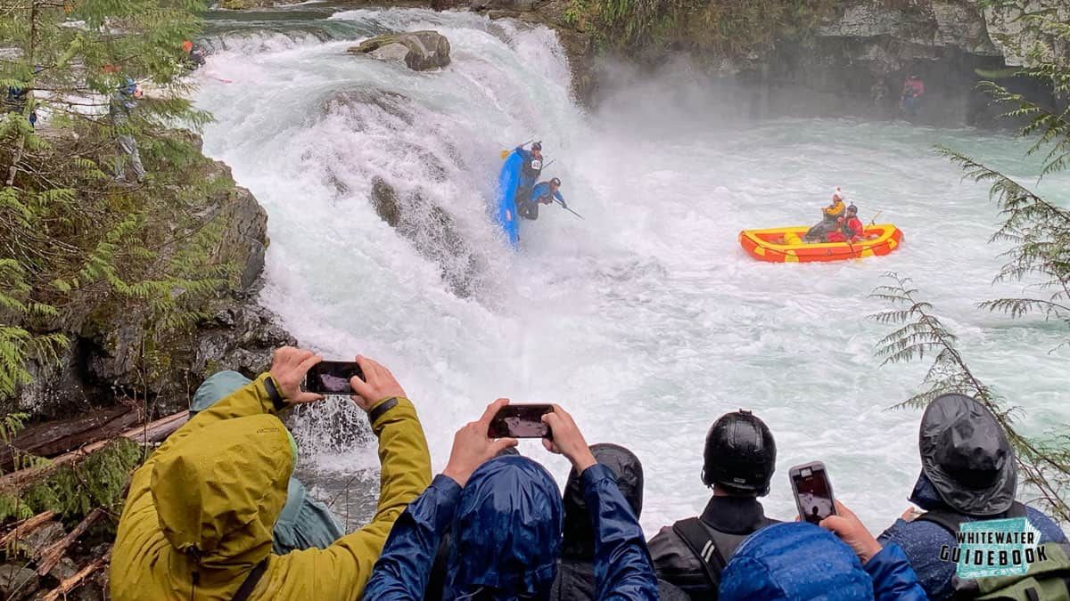 A group of people are taking pictures of a person in a raft in a river. A group of people are taking pictures of a person in a raft in a river.