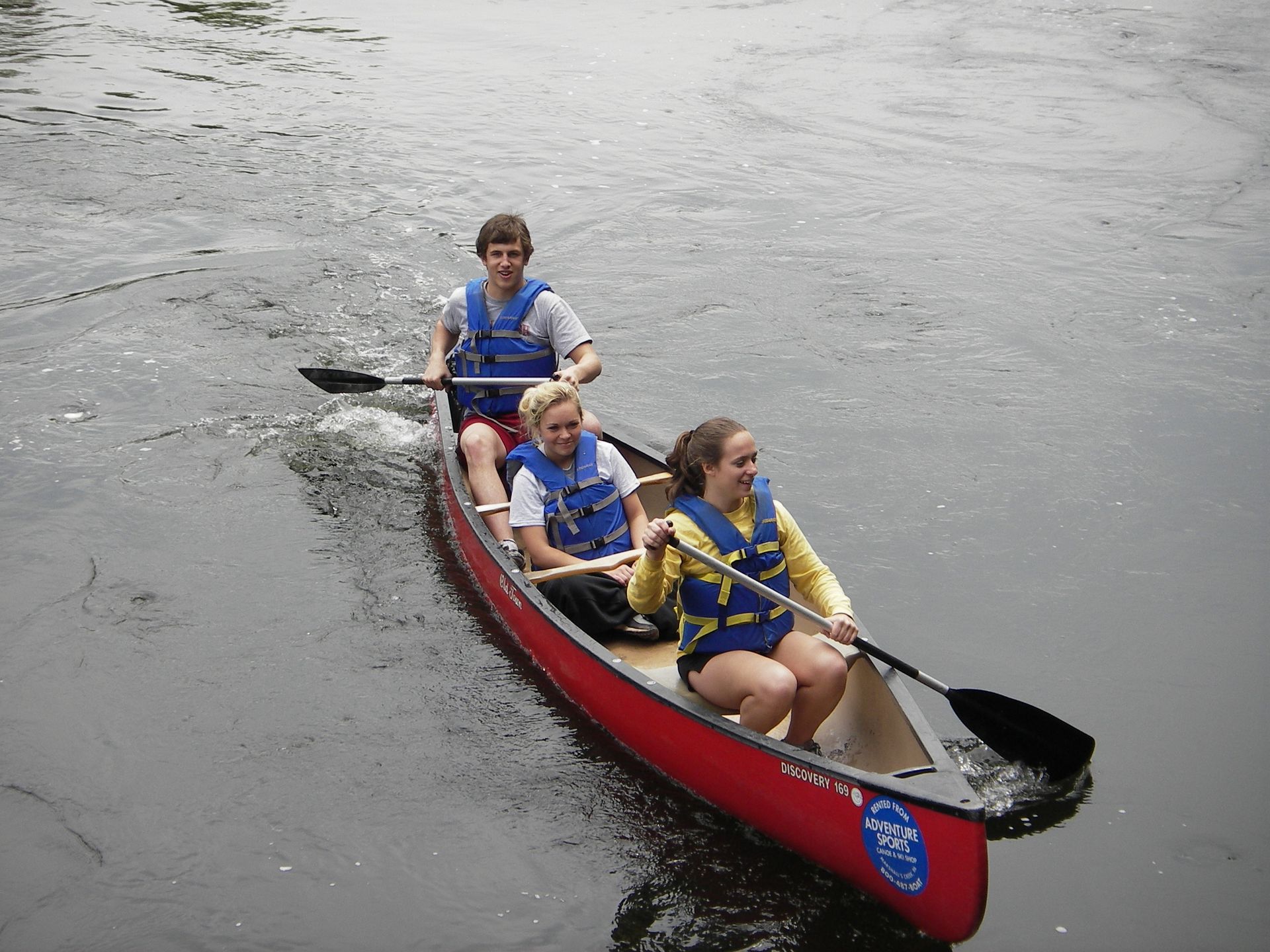 Three people are in a red adventure sports canoe on a river