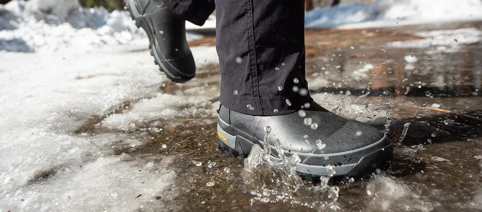A person wearing black river boots is walking through a puddle of water. A person wearing black river boots is walking through a puddle of water.