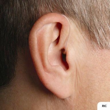 Primer plano de la oreja de un hombre con un audífono con receptor en el canal auditivo (RIC). El cable delgado va desde el audífono detrás de la oreja hasta el canal auditivo.