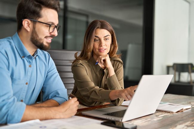 Two coworkers collaborating at a desk with a laptop in a bright office