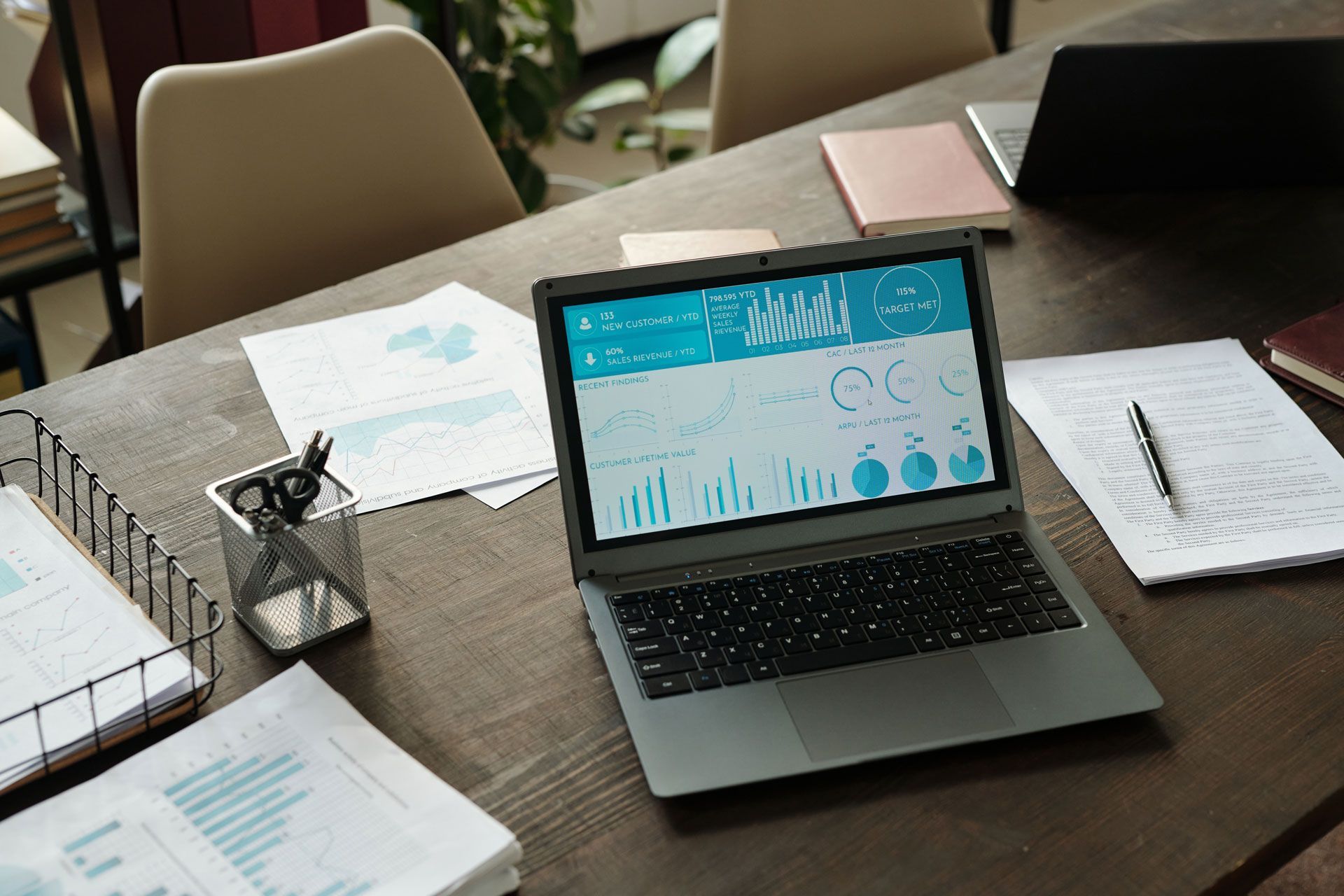 Laptop on office desk showing analytics charts, with papers, notebook, and pen nearby