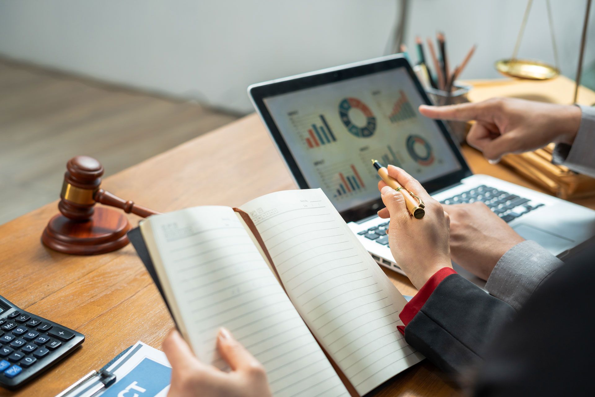 Lawyer reviewing charts on a laptop beside an open ledger and gavel on a desk