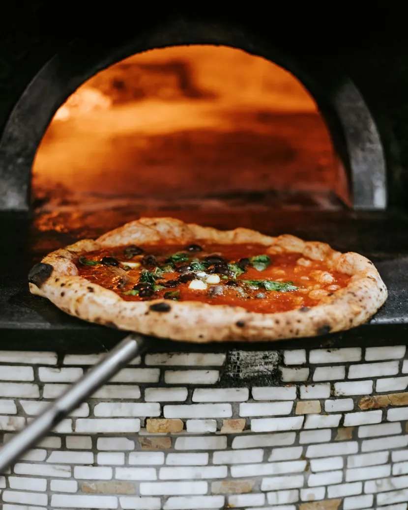 A thin-crust pizza topped with cured ham, sitting on a wooden platter