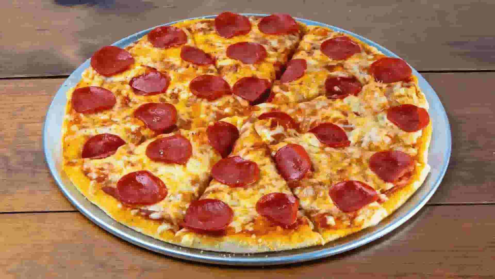 A sliced pepperoni pizza with melted cheese on a round metal pan sits on a wooden surface.